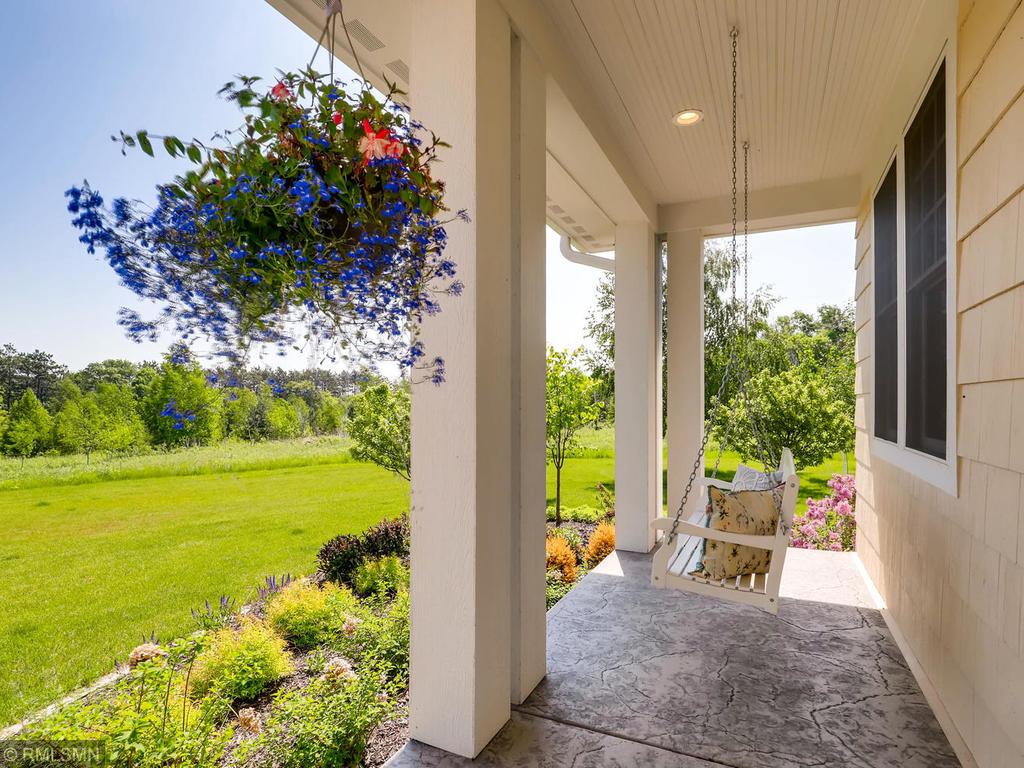 Summer flowers and landscaping by porch with cream wooden country swing.