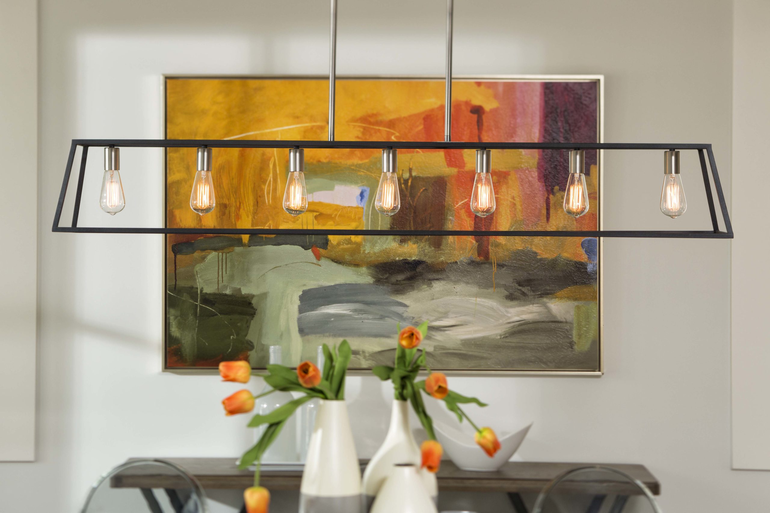 Variety of dining room accessories including modern light fixture, bright orange and green painting with flowers is vases to match.