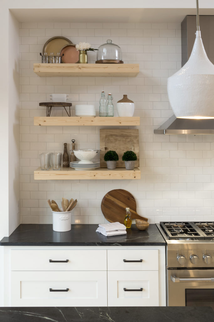 A white kitchen with black counter tops and wooden shelves.
