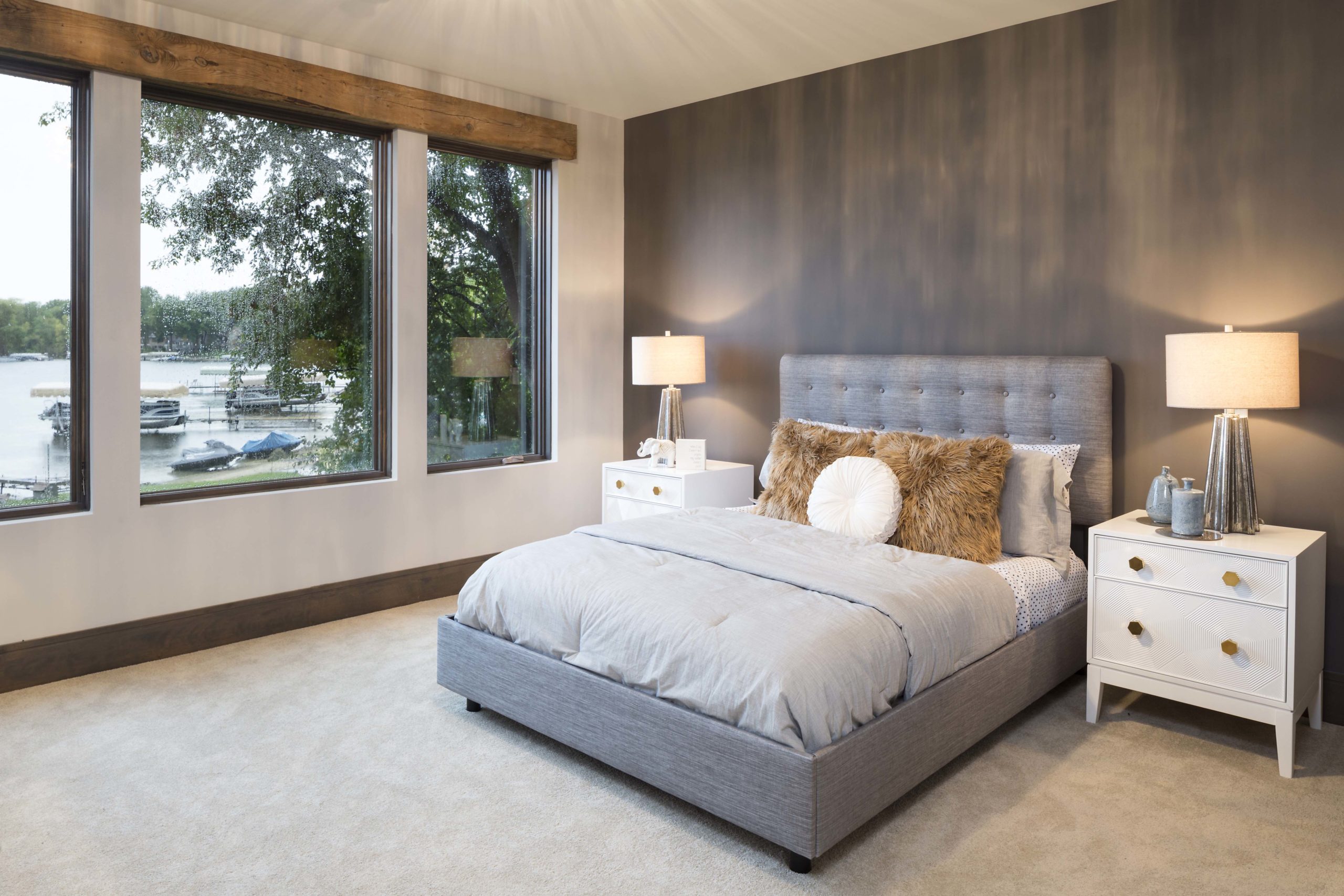 Large master suite with dark gray accent wall, light gray decorative bedding and cream night stands with lamps.