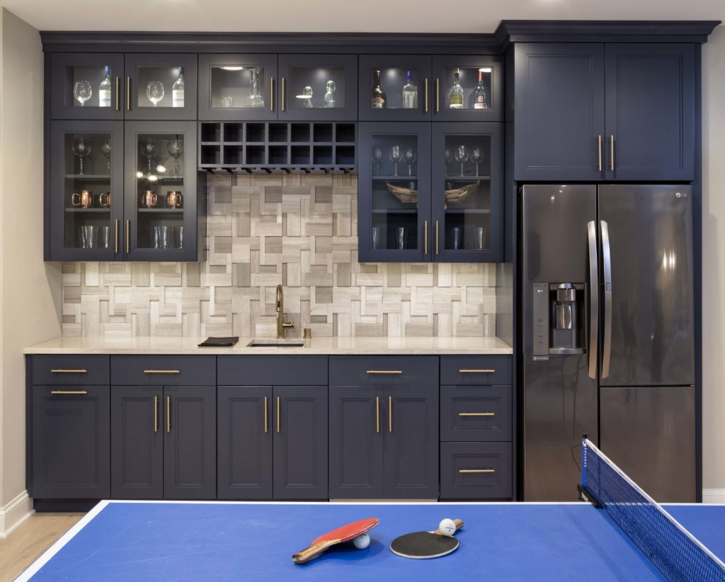 Dark wood wet bar showcasing glass front cupboards displaying bottles and glasses near a blue pingpong table.