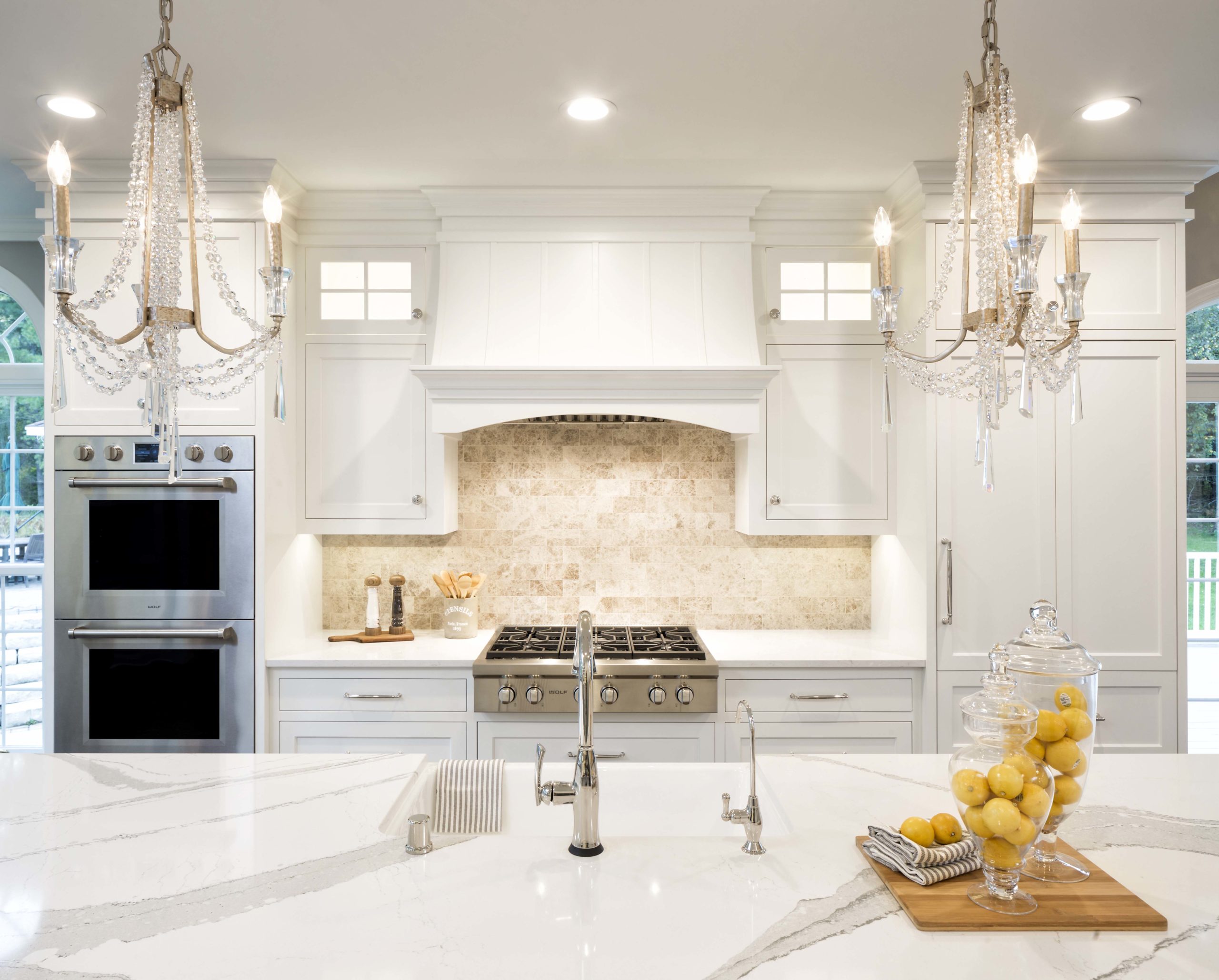 A white kitchen with marble counter tops and a chandelier.
