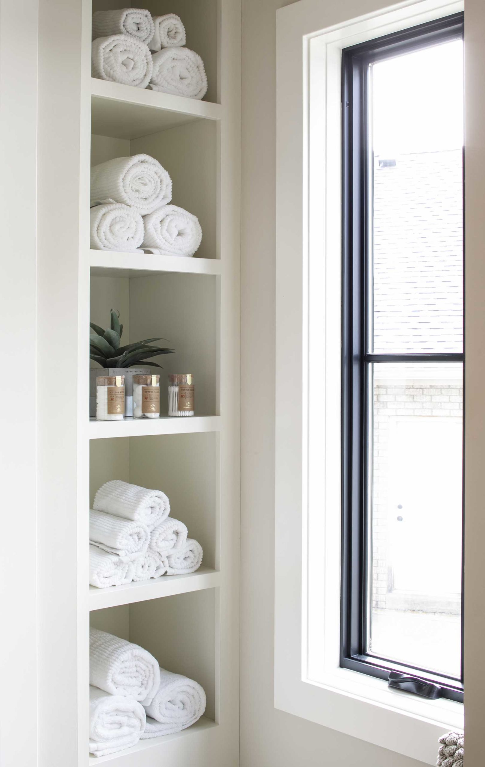 A bathroom with a shelf full of towels next to a window.