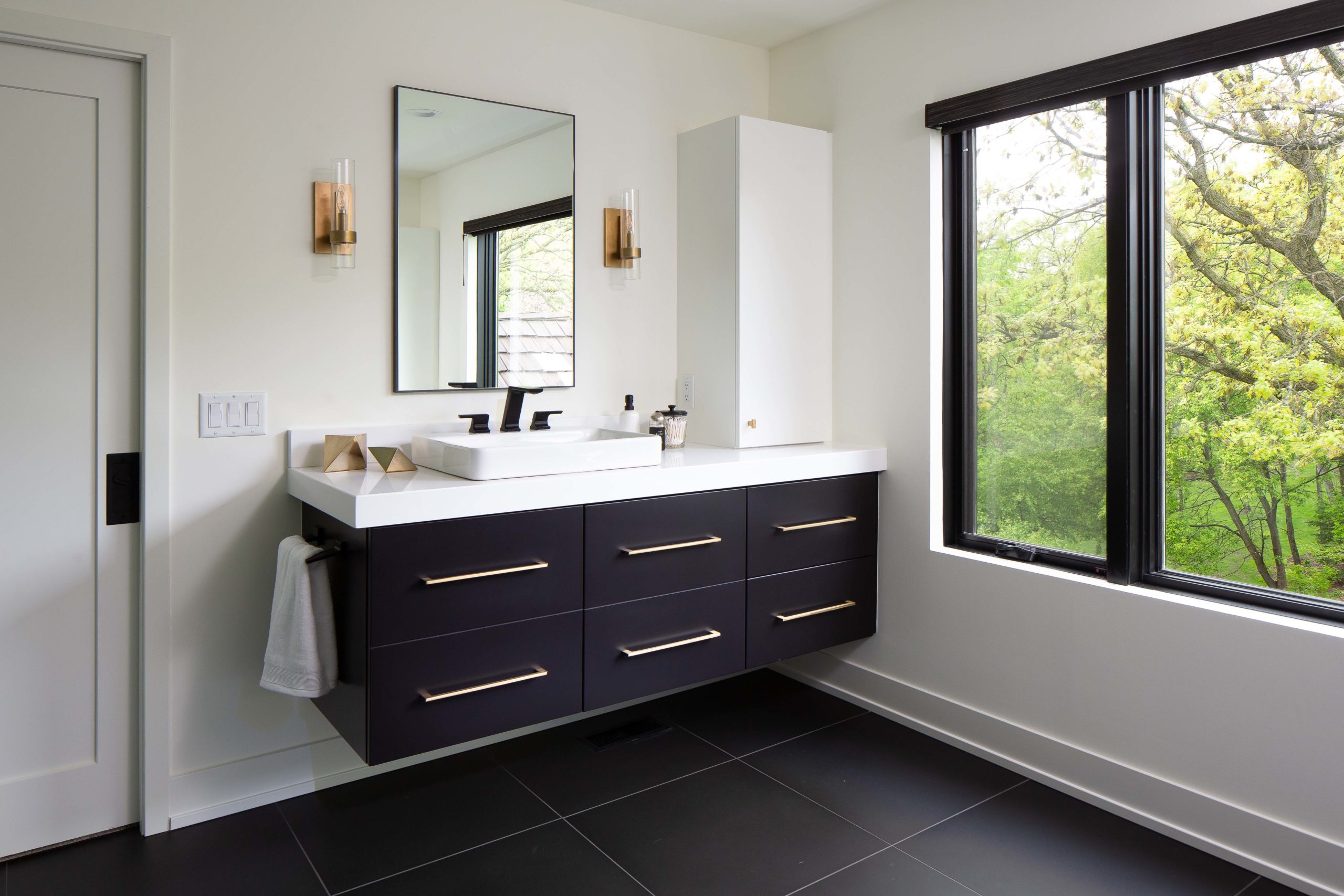A modern bathroom with black cabinets and a window.