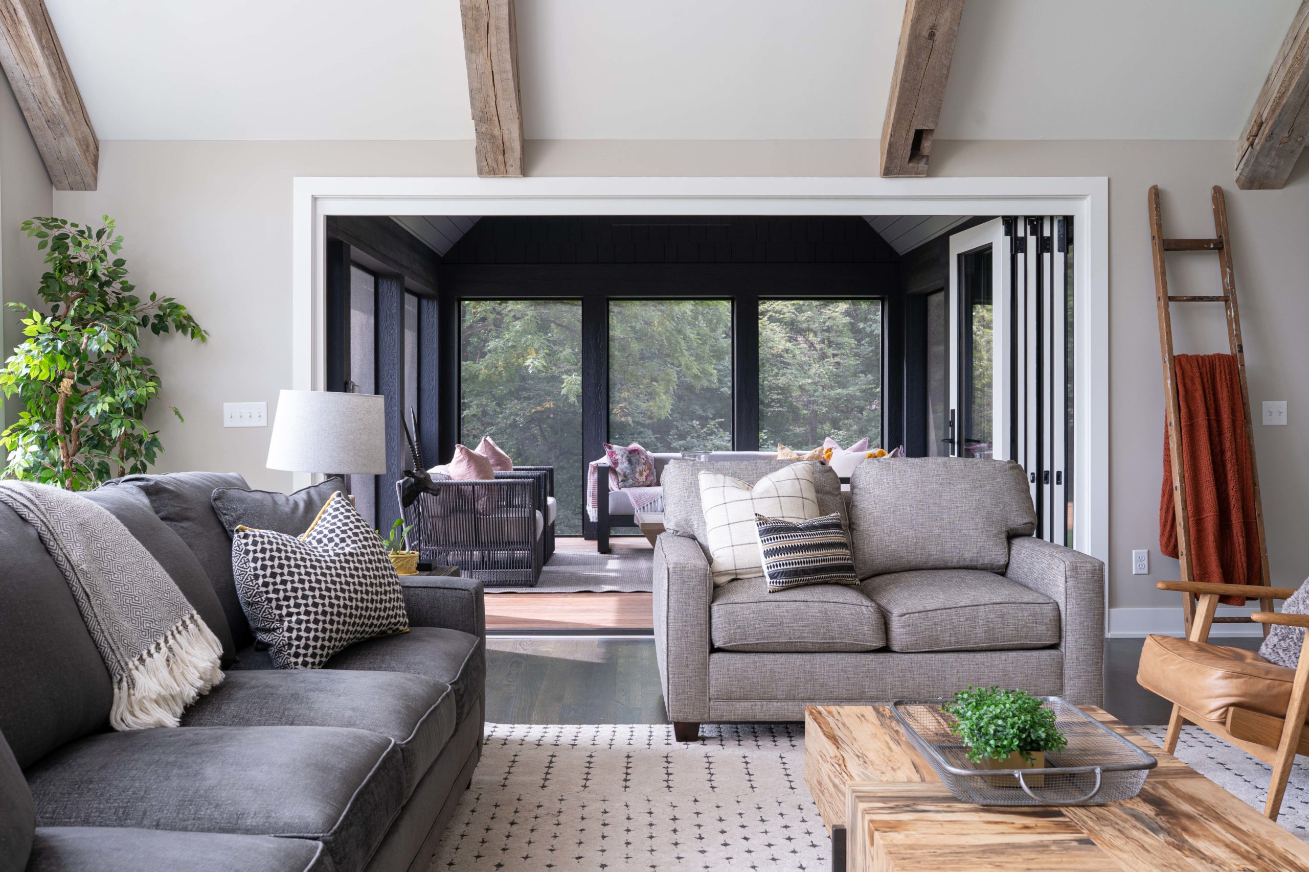 A living room with gray furniture and wooden beams.