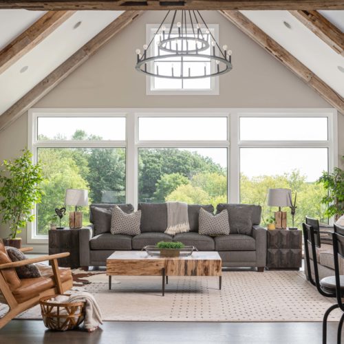 A living room with large windows and wood beams.