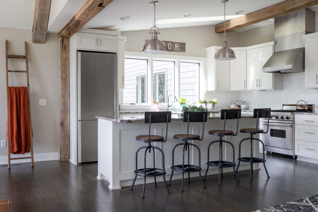 A white kitchen with wooden beams and stools.