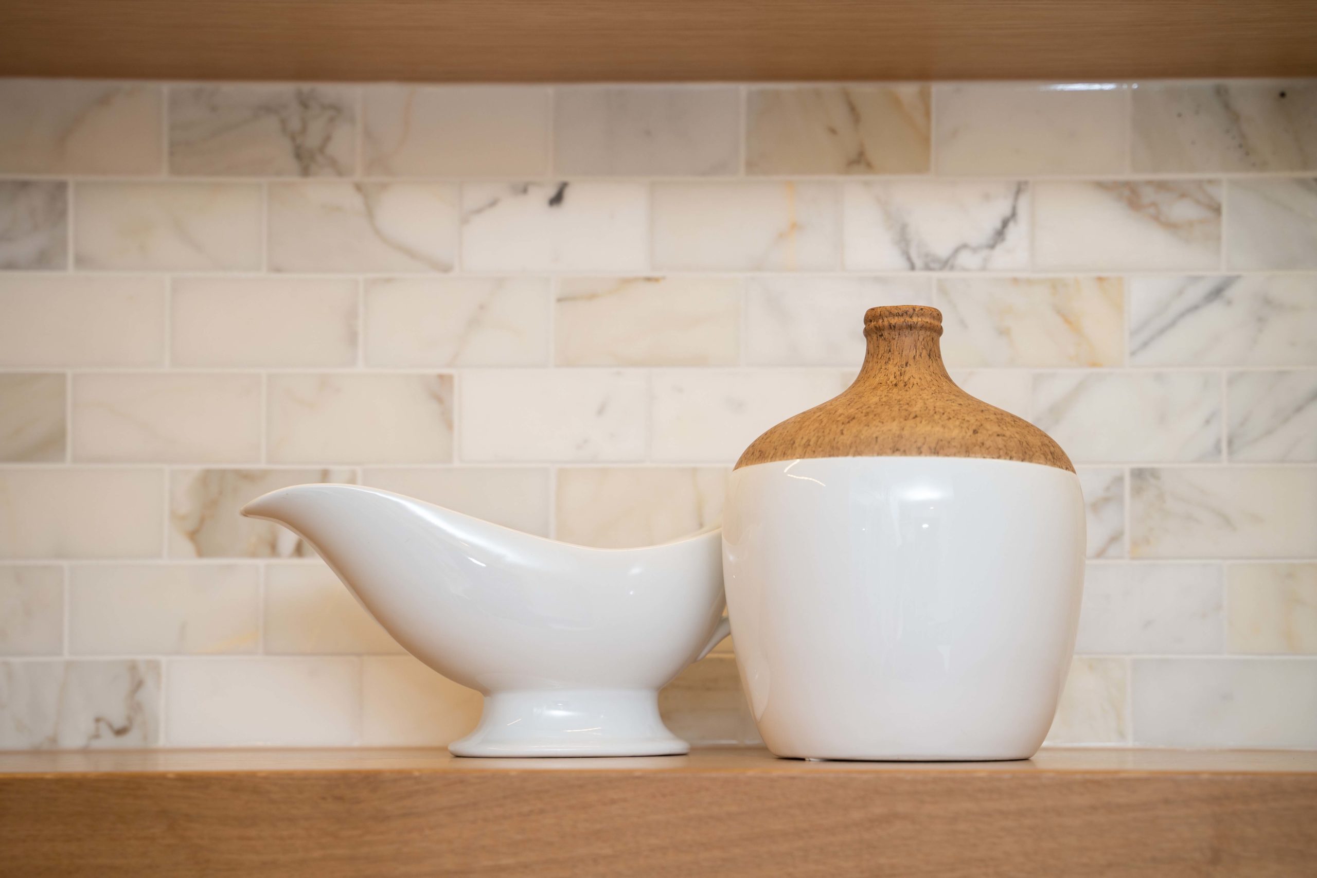 White gravy bowl and vase on wood shelf in kitchen.