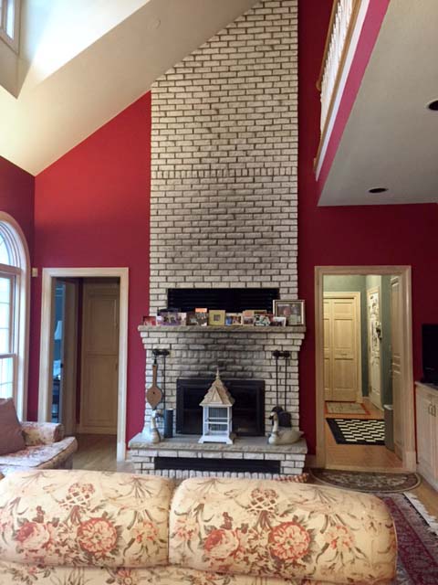 A living room with red walls and a brick fireplace.