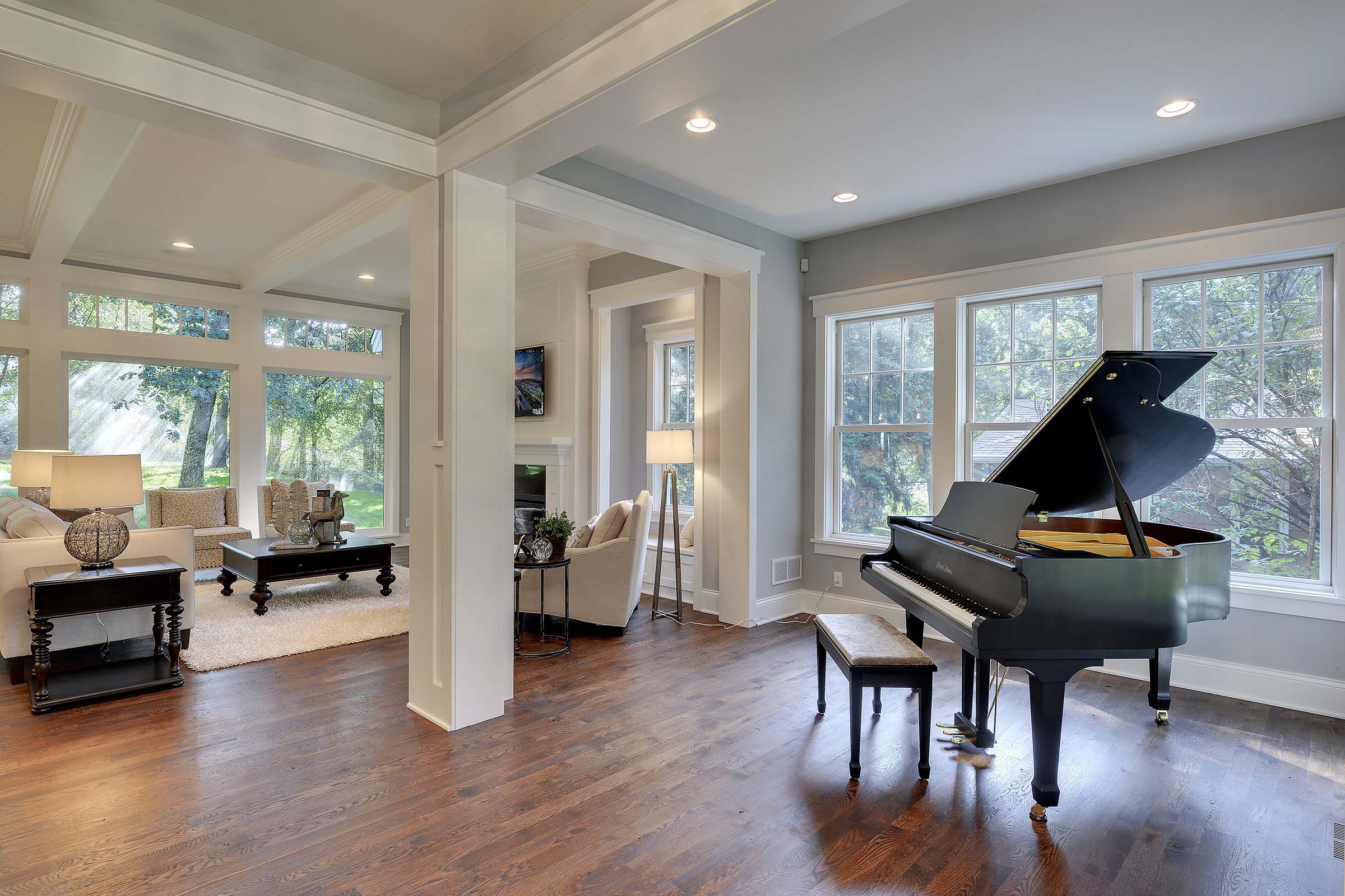 Piano area open into living room with high ceilings, wood floors and multiple windows.