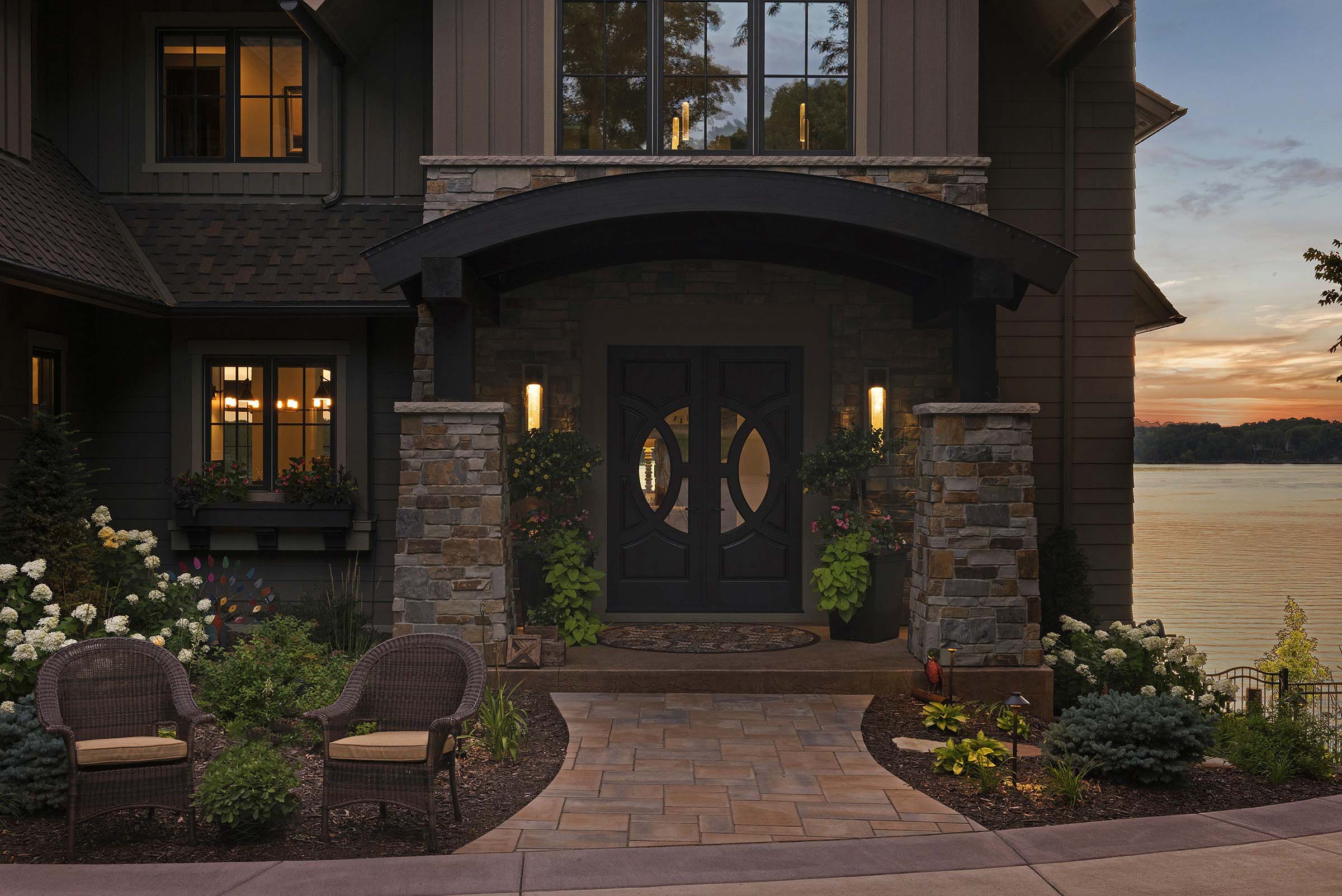 Front entrance with elegant brown detailed doors, arched awning and beautiful flowers.