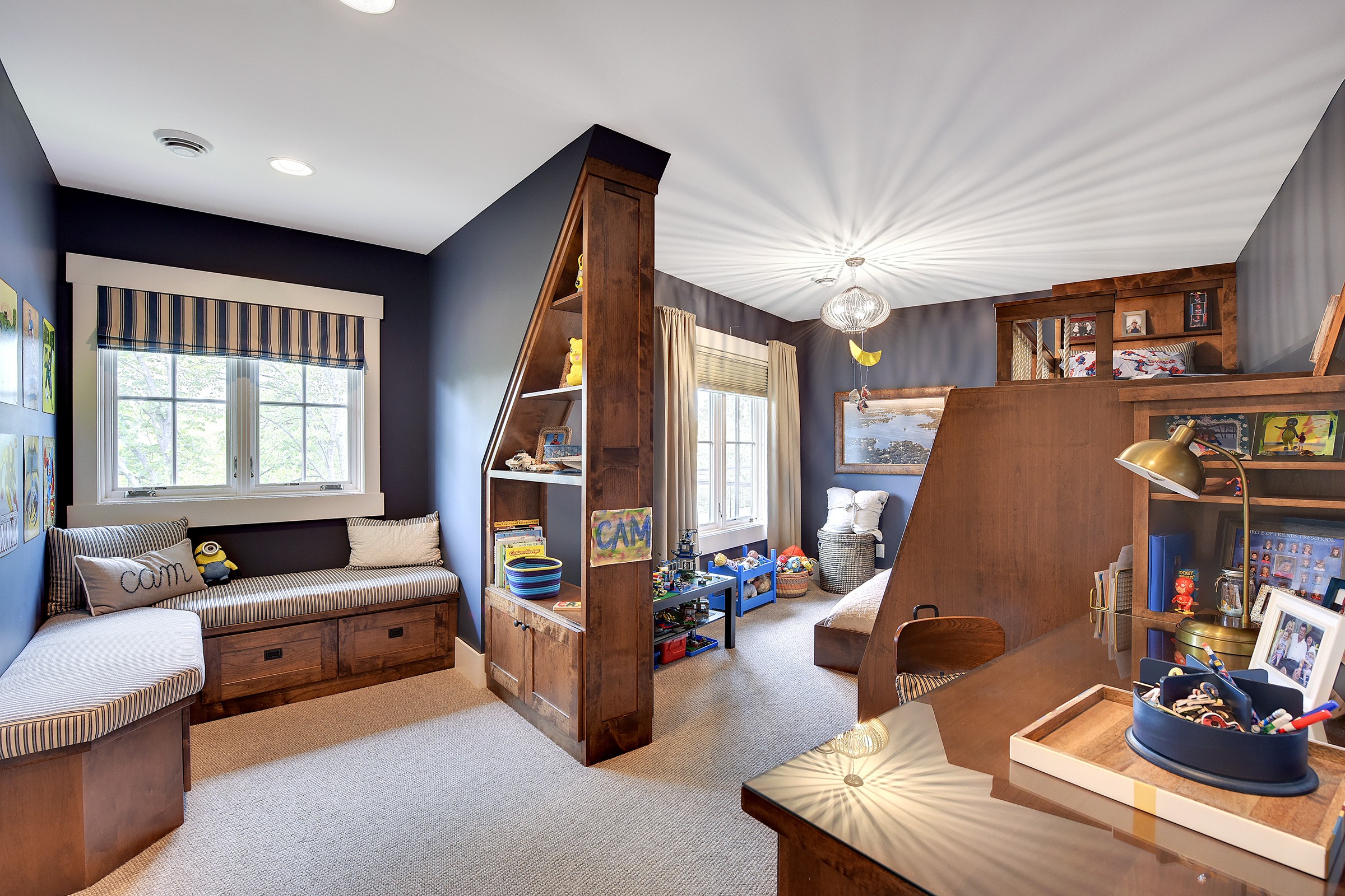 Dark blue child's bedroom with cushioned window bench, desk and shelving areas for toys.
