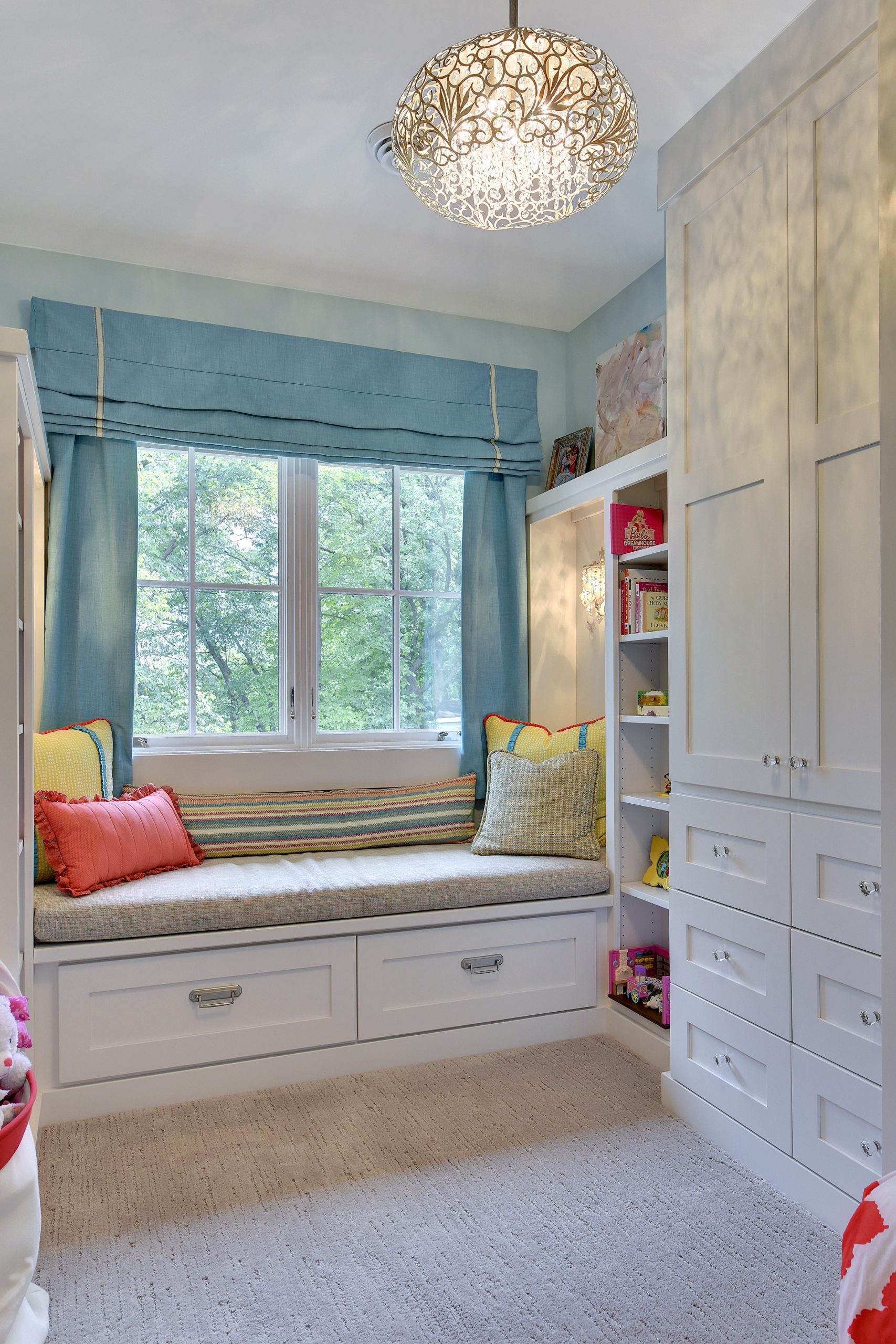 Pastel blue bedroom with cushioned bench drawers by window, spring like colorful accents and white builtin cabinet.