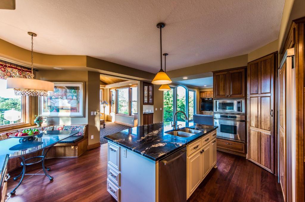 Open kitchen and dining area with dark hardwood floors, granite countertop and rich wood cupboards.