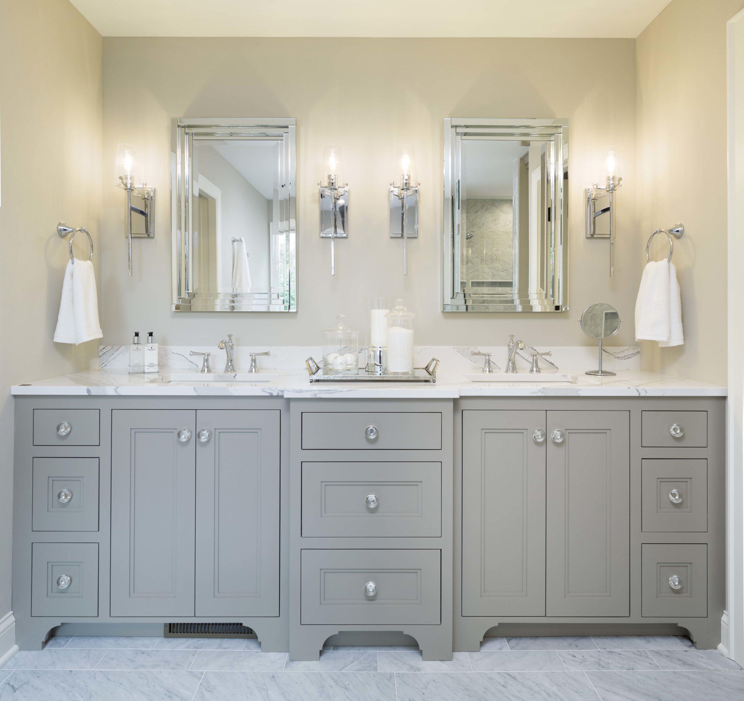 A bathroom with gray cabinets and mirrors.