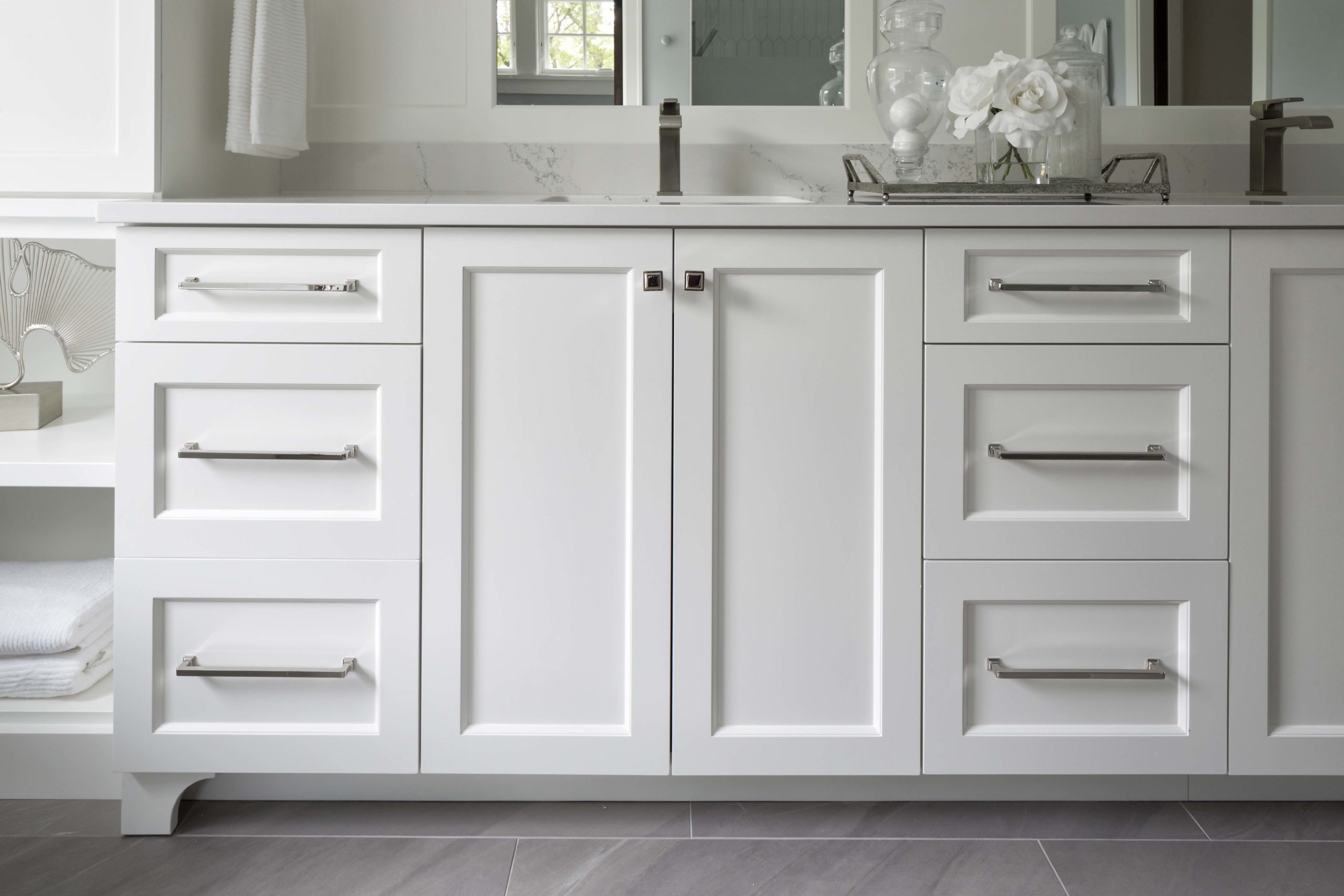 A bathroom with white cabinets and a mirror.