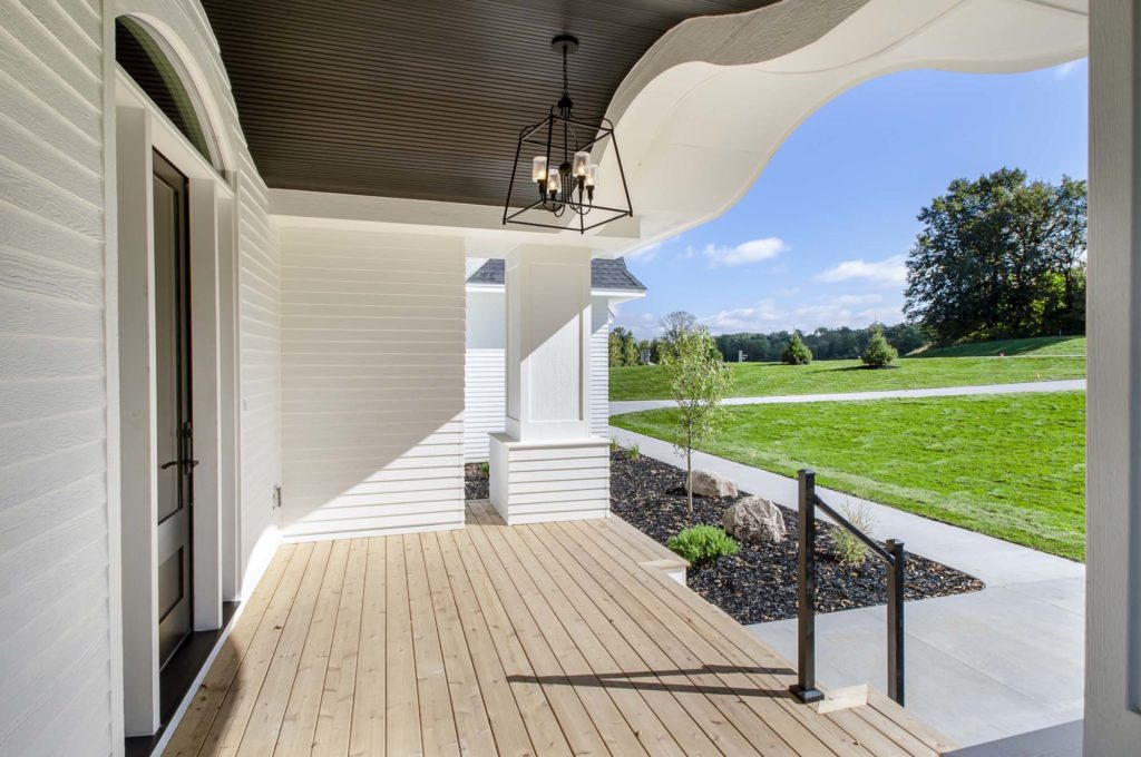 The front porch of a home has a white railing and a light fixture.