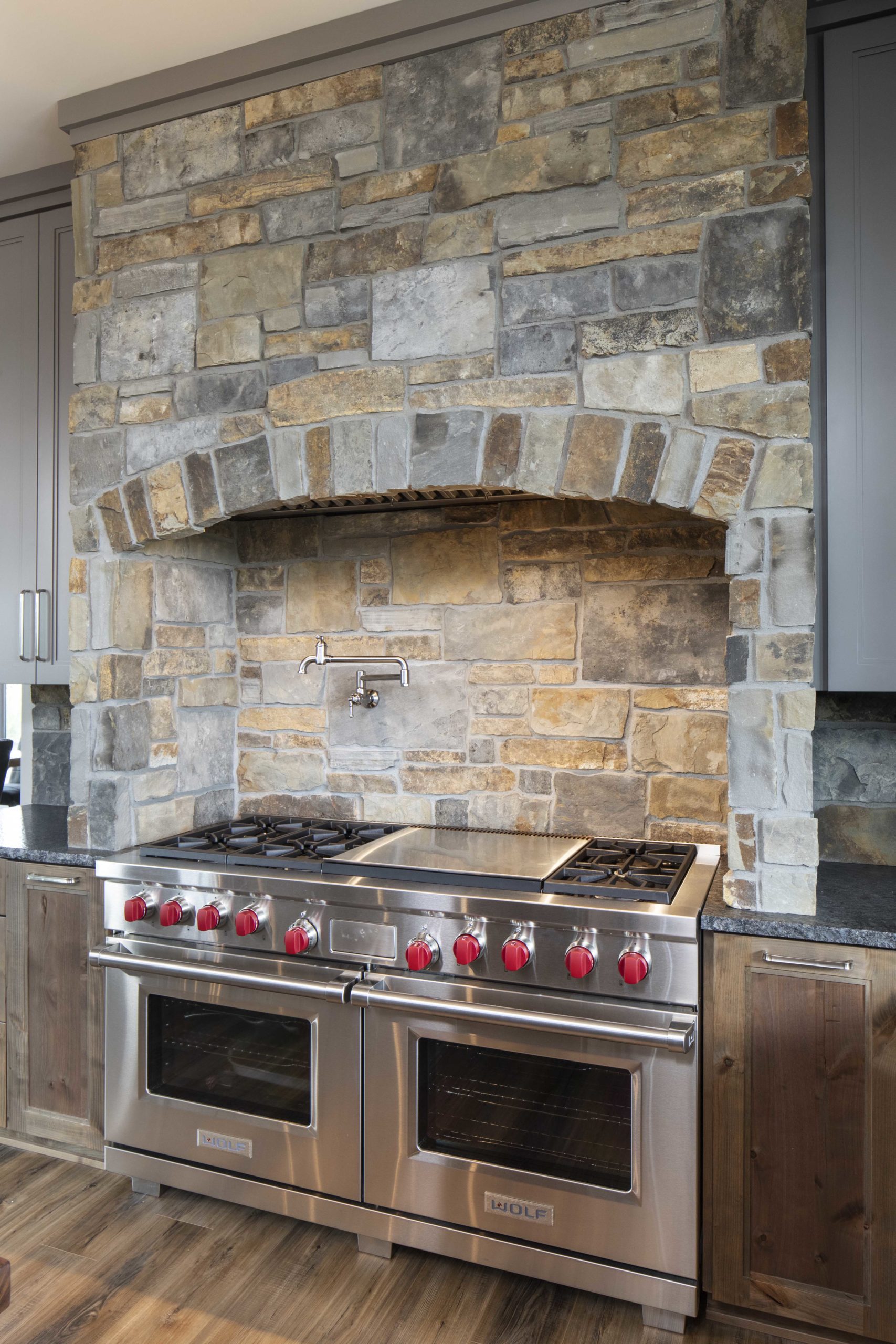 A kitchen with a stone wall and stainless steel appliances.