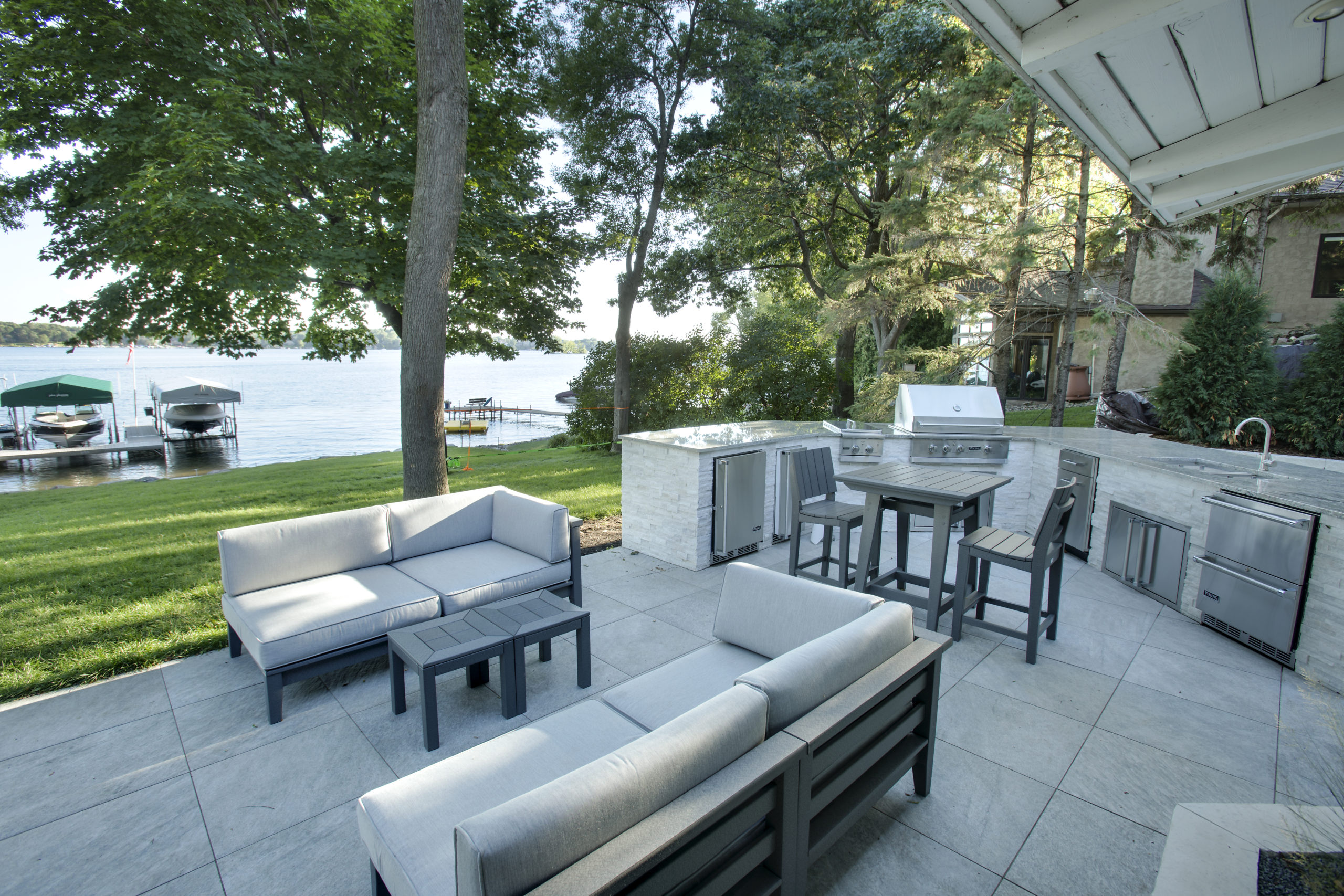 A patio with a grill and furniture near a lake.