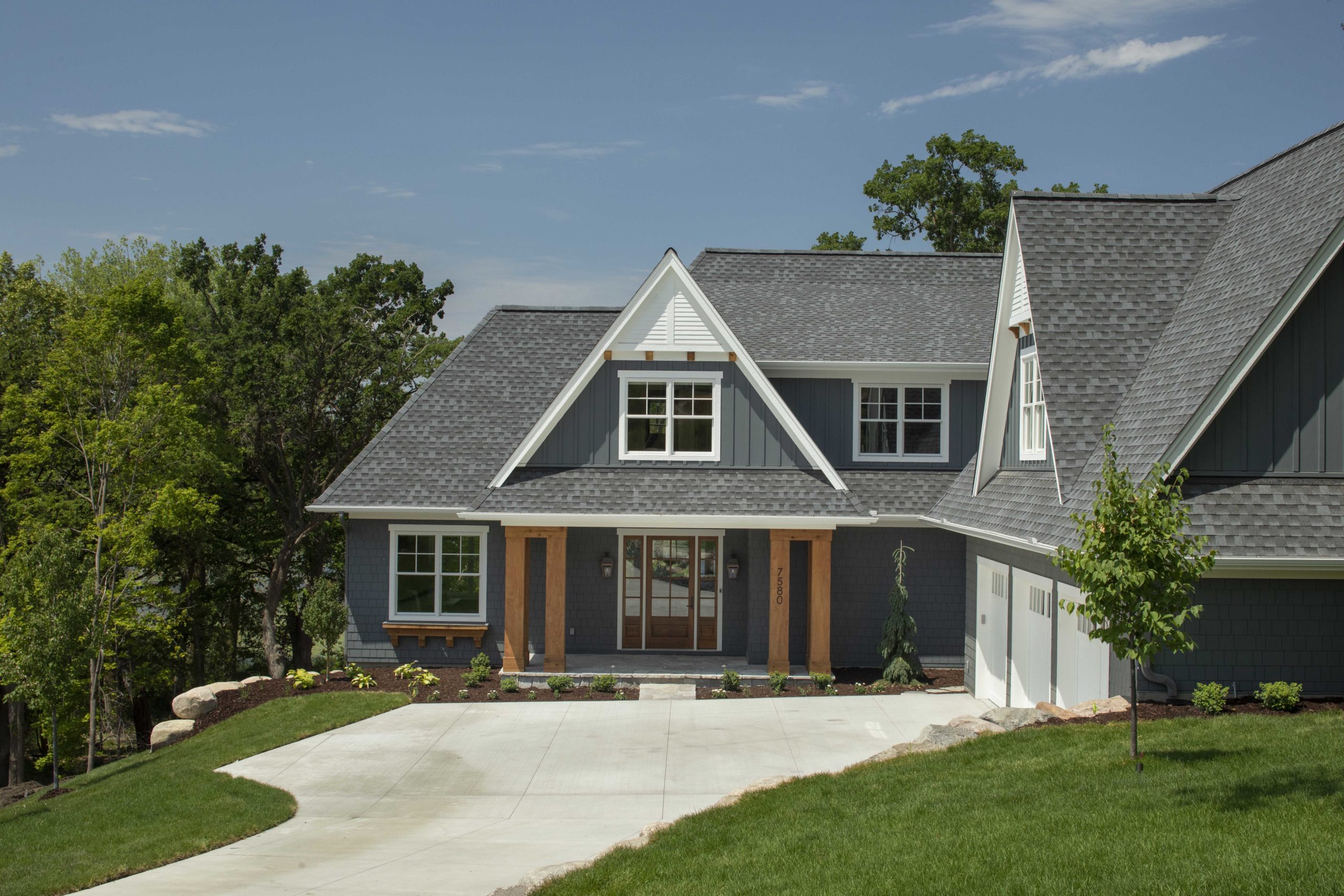 A custom home with a gray exterior, situated by a lake, and featuring a driveway.