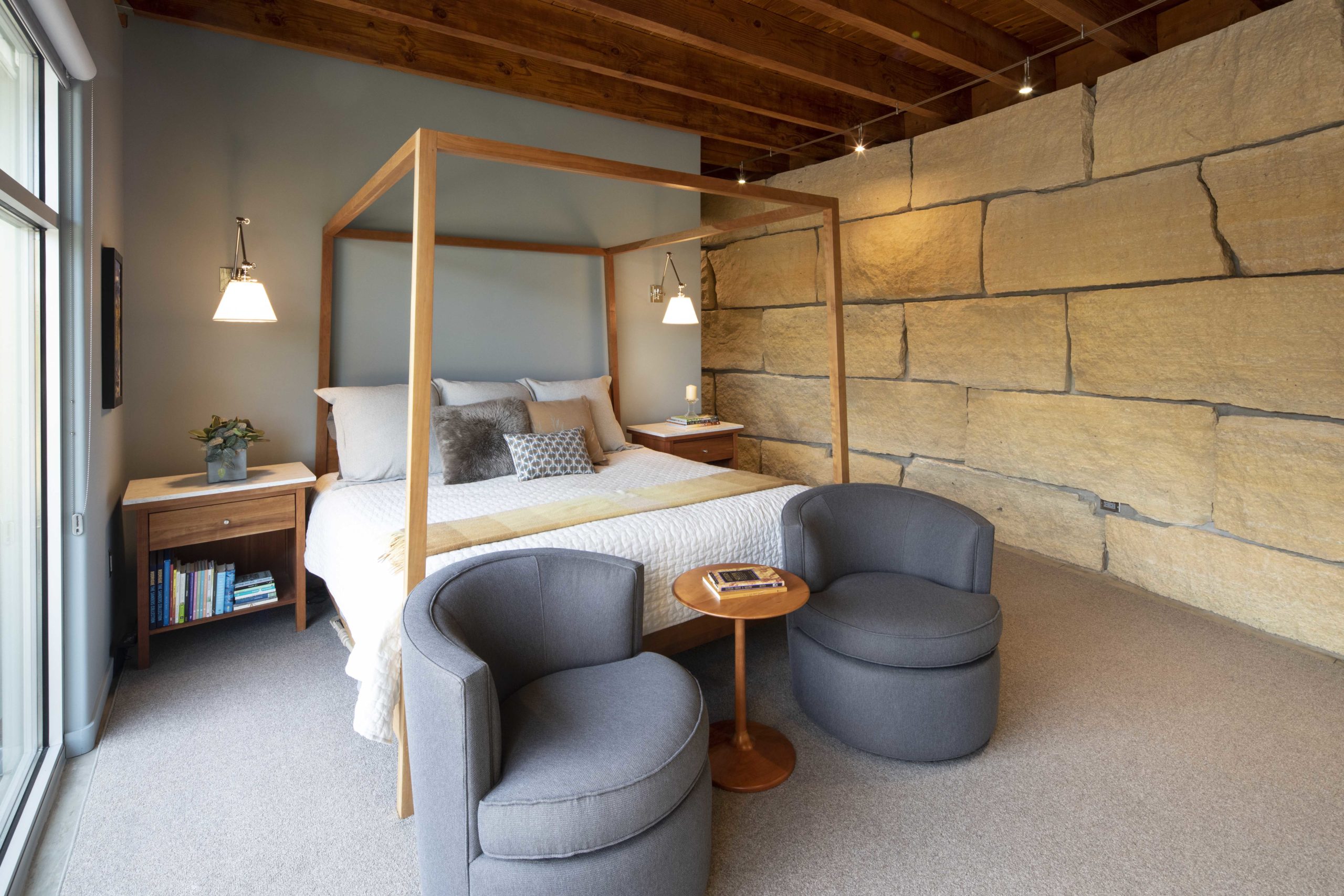 A contemporary four poster bed in a bedroom with stone walls.