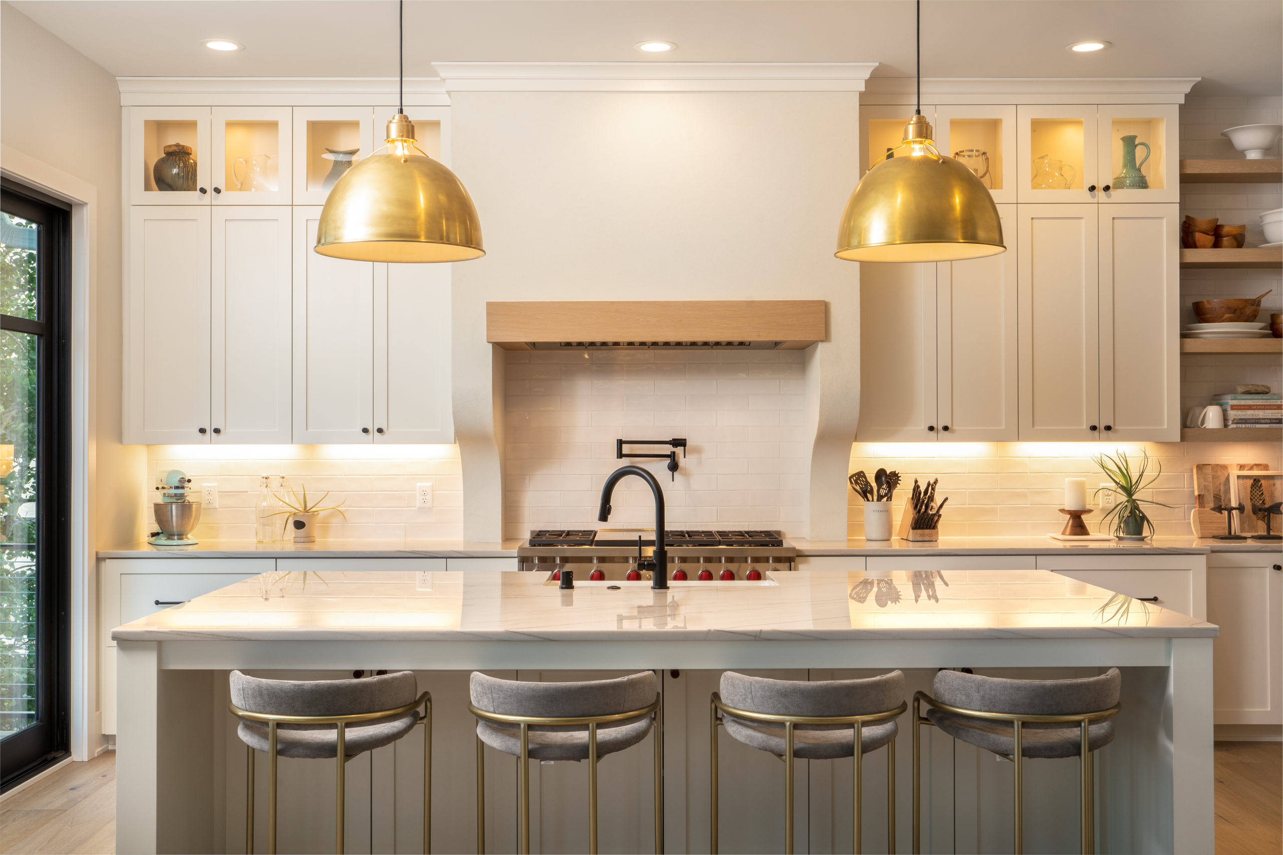 A white kitchen with gold pendant lights and stools.