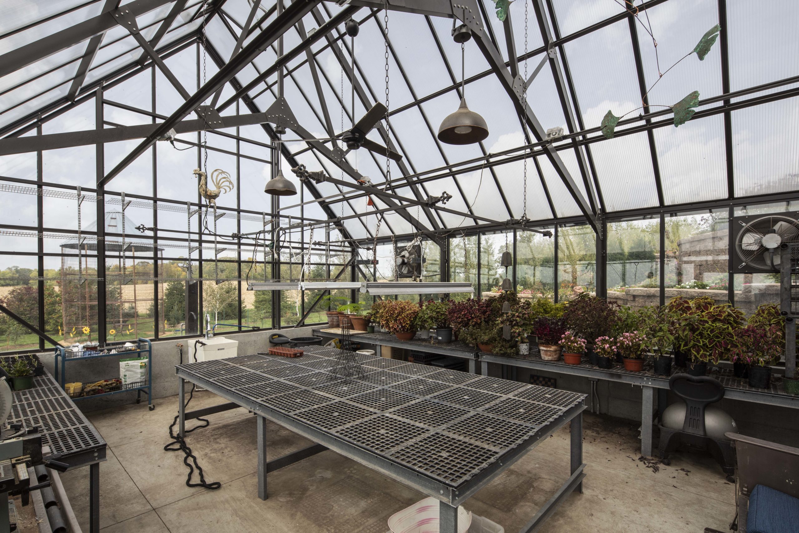 A prairie-style greenhouse, adorned with a variety of plants, features a table for display and cultivation.