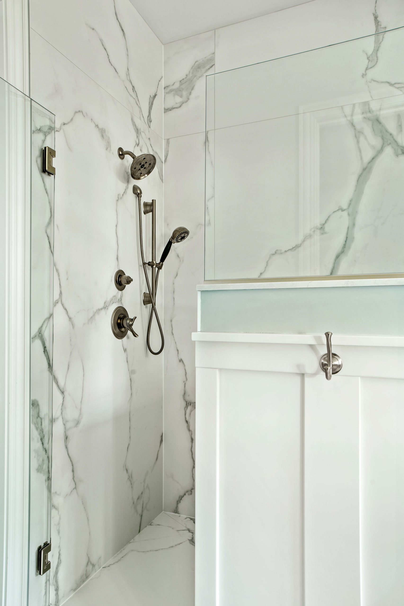 The Lake Escape custom home remodel features a white bathroom with marble walls and a glass shower door.