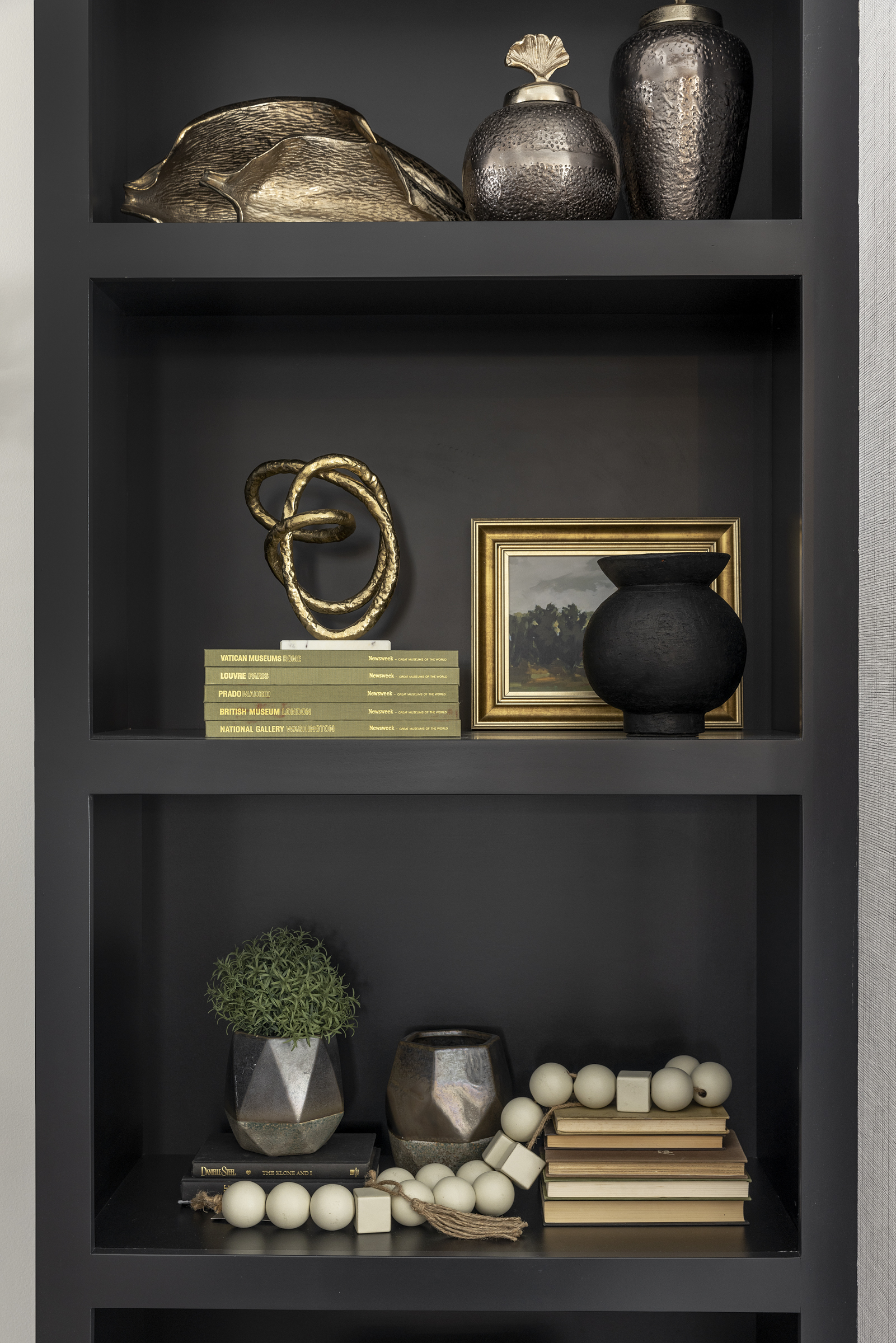 A black bookcase with gold vases on it.
