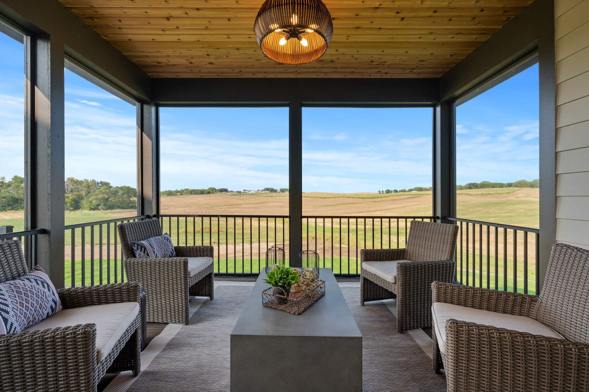 A screened porch with wicker furniture and a view of a prairie field.