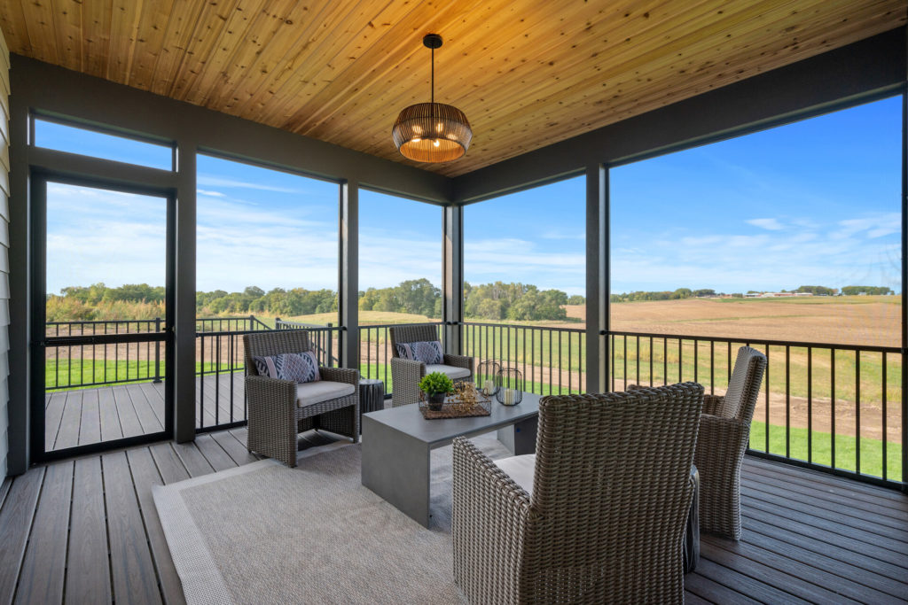 A prairie-style screened in porch with wicker furniture and a view of a field.