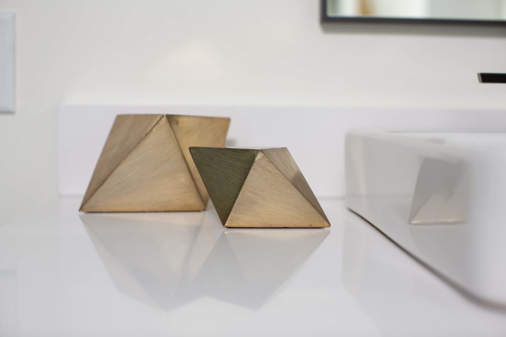 Two gold triangles sit on top of a modern bathroom counter.