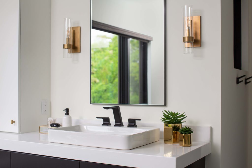A modern bathroom with a sink and mirror that has undergone a remodel.