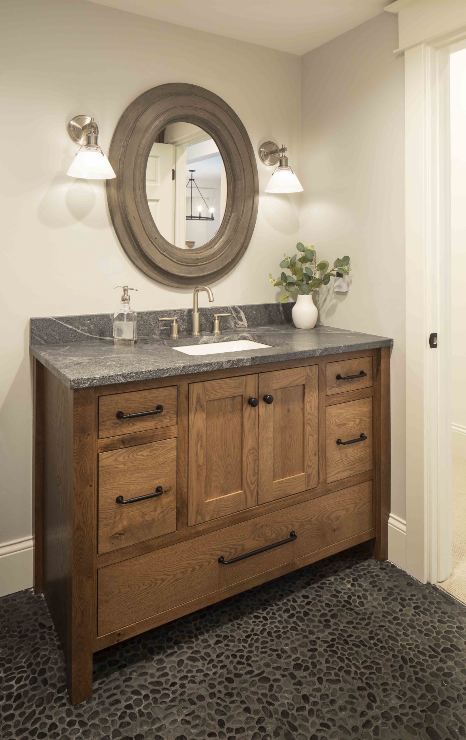A prairie-style bathroom with a wooden vanity and a round mirror in a custom home.