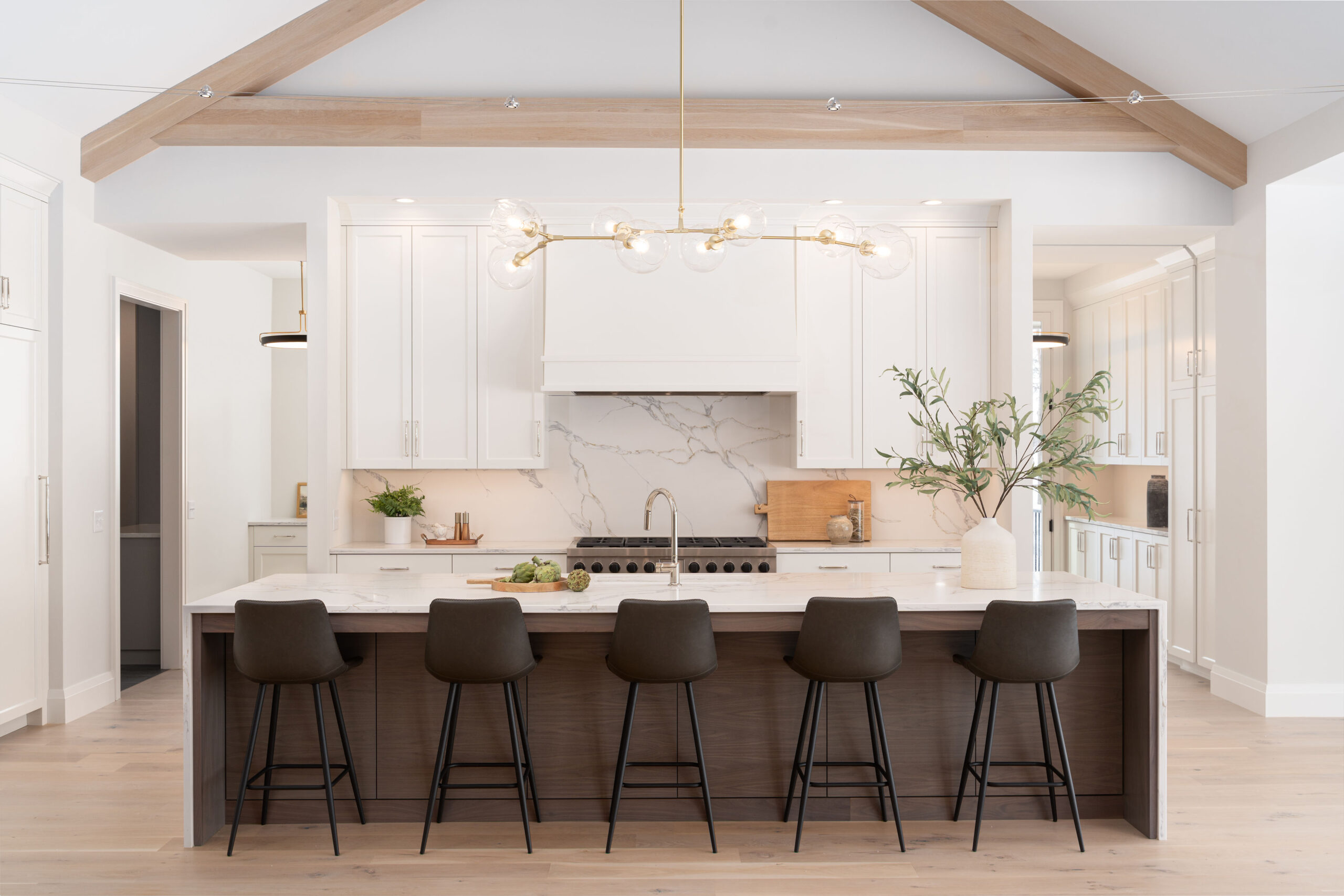 A white kitchen with wood beams and black stools.