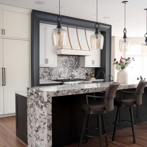 A modern kitchen with marble counter tops and stools.