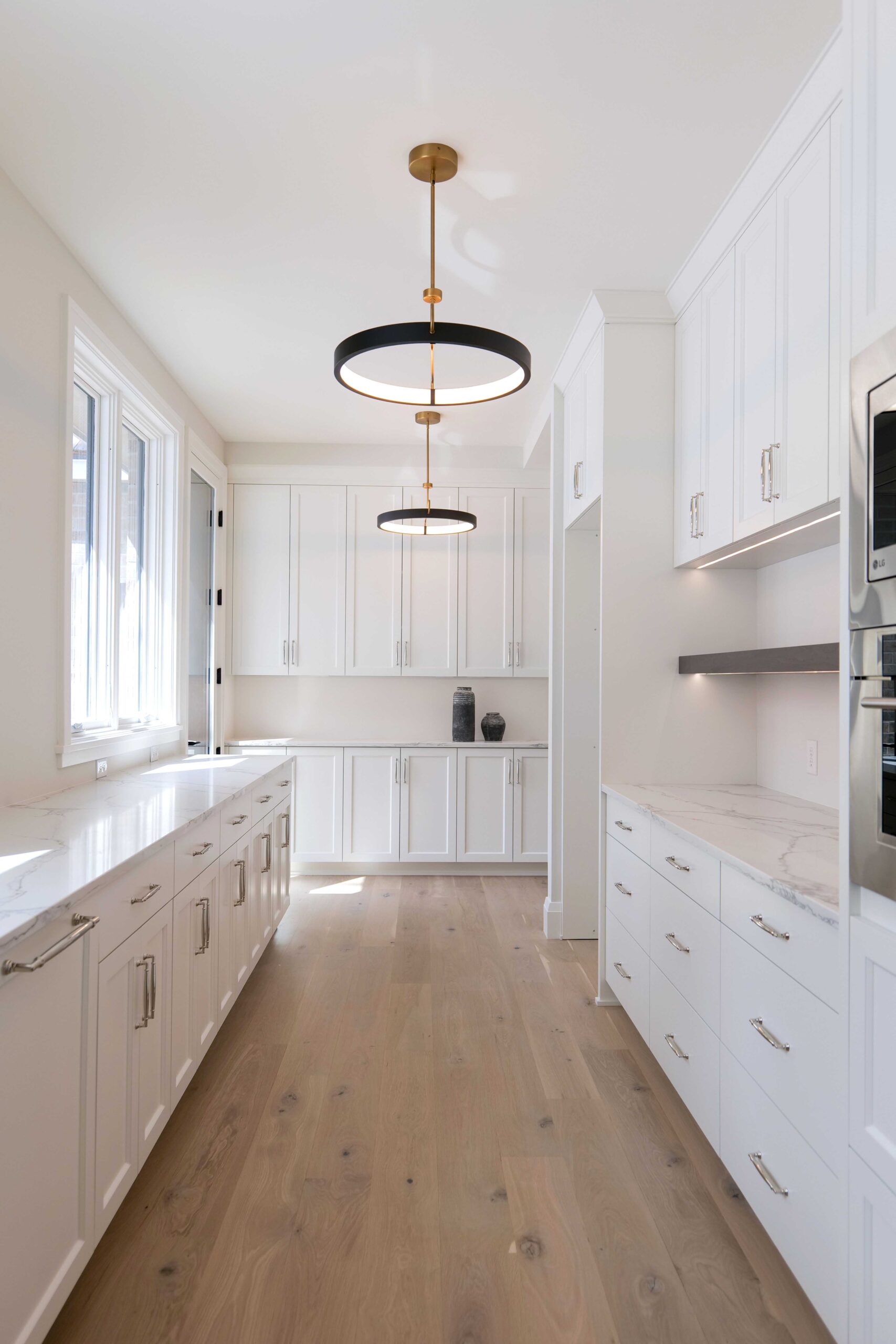A white kitchen with hardwood floors and a pendant light.
