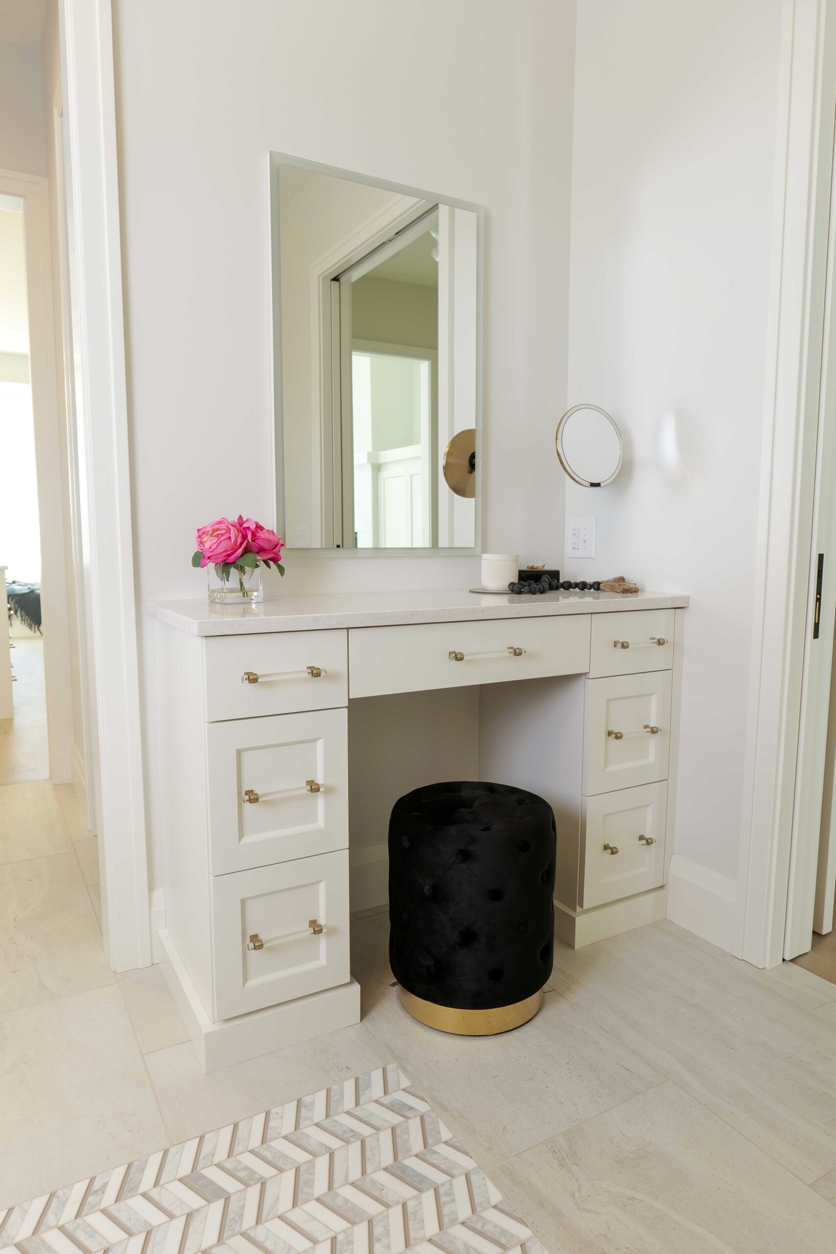 A white vanity with gold accents and a black ottoman.