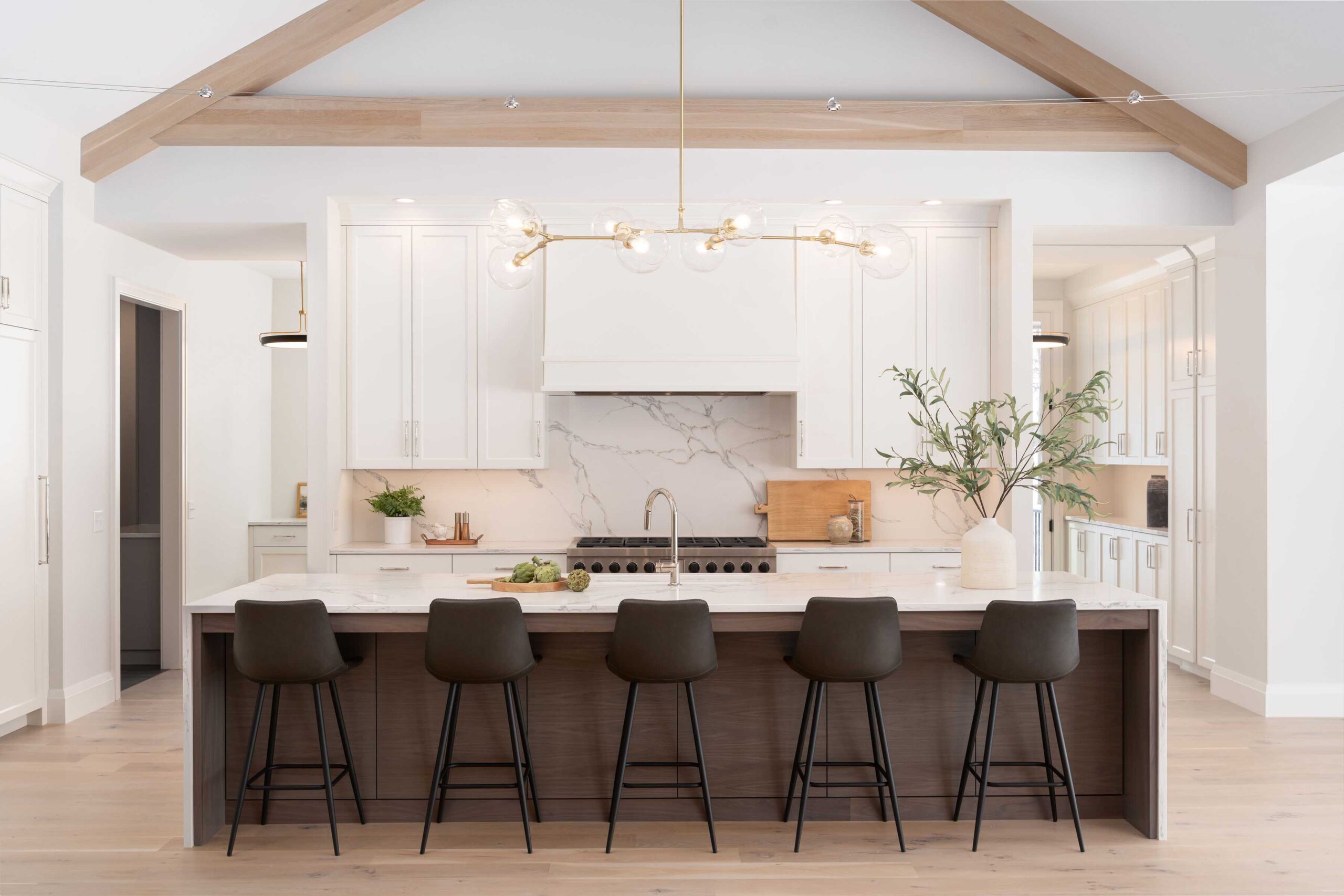 A white kitchen with wooden beams and black stools.