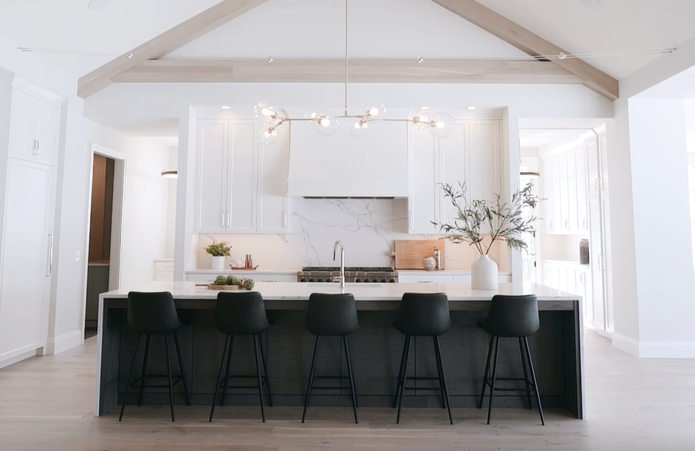 A white kitchen with black stools and a wooden ceiling, perfect for a Woodside remodel.