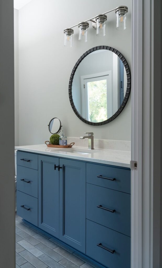A transitional bathroom with blue cabinets and a mirror.