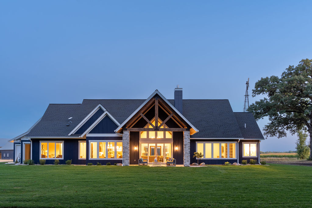 A transitional farmhouse with a blue exterior and large windows.