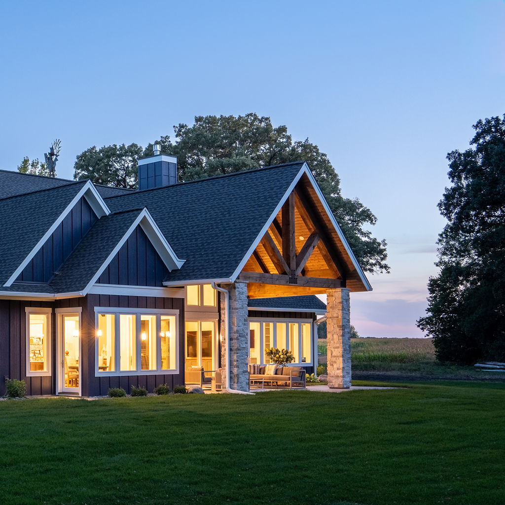 A transitional farmhouse with a large front porch and large windows.