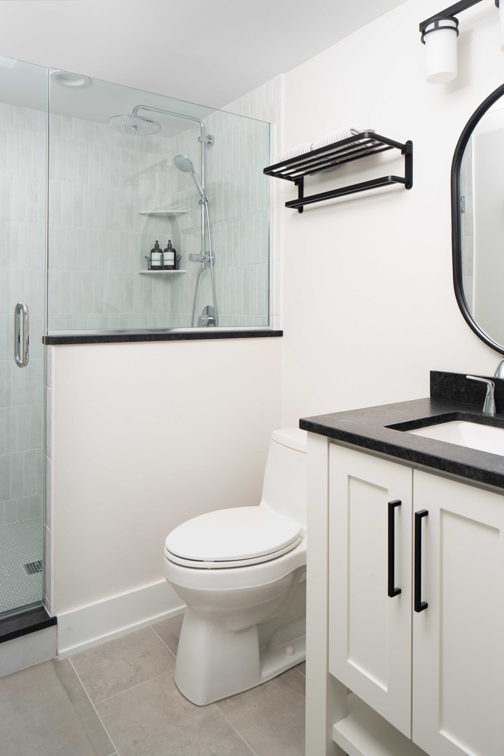 The Orchard Lake Remodel features a stylish black and white bathroom with a sleek glass shower stall.