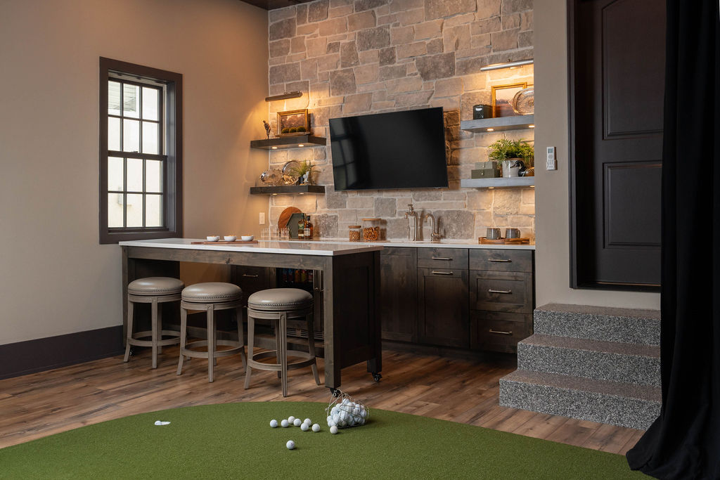 Modern kitchen with stone wall accent, including built-in shelves and TV, adjacent to indoor putting green featuring a golf simulator and bar remodel.
