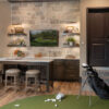 Modern home office with a golf simulator, stone accent wall, and dark wood features.