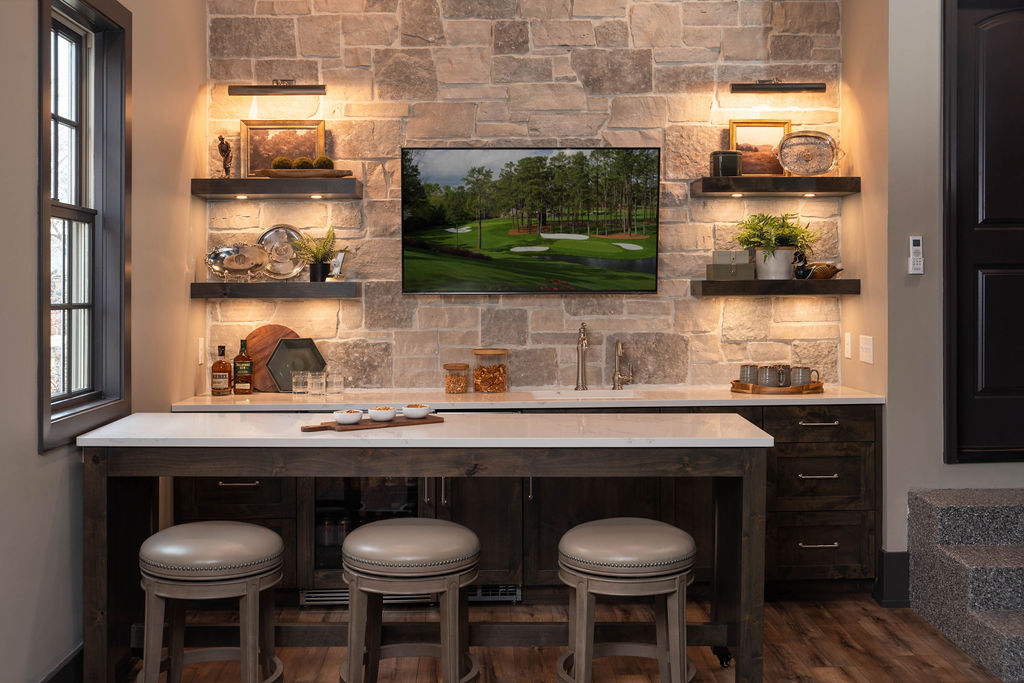 Modern kitchenette with stone wall, mounted television, bar seating, and golf simulator.