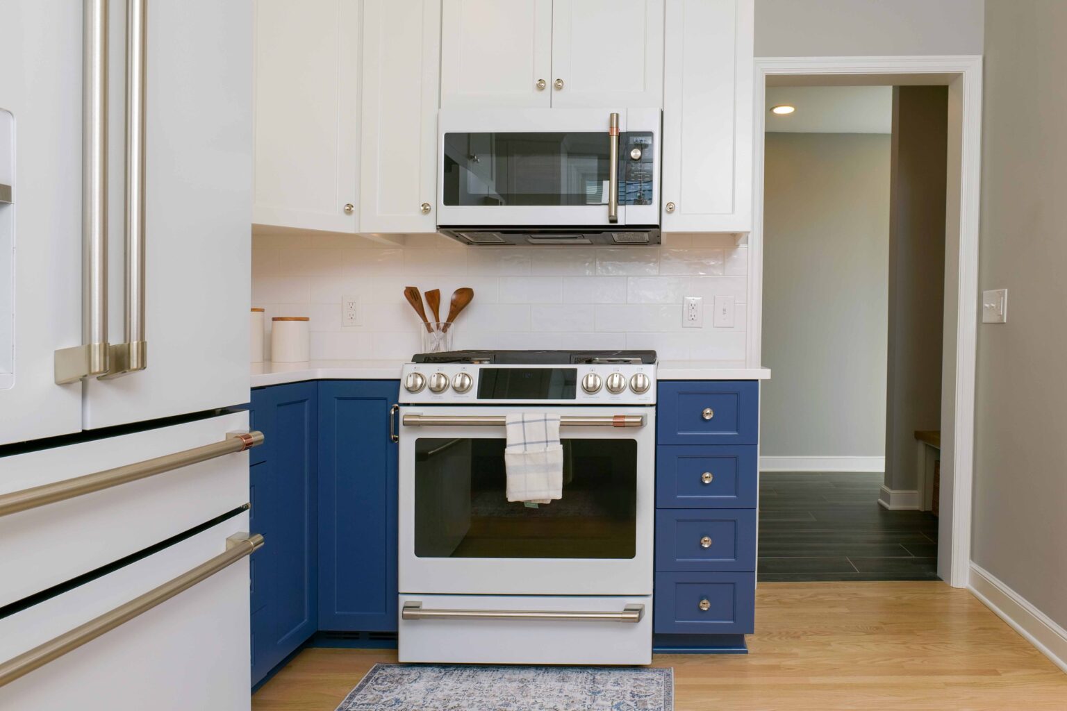 A modern kitchen on Hampshire Drive features a white and blue color scheme, with a white refrigerator, blue lower cabinets, a white oven with a towel hanging, and a white microwave above. This remodel seamlessly blends style and functionality.