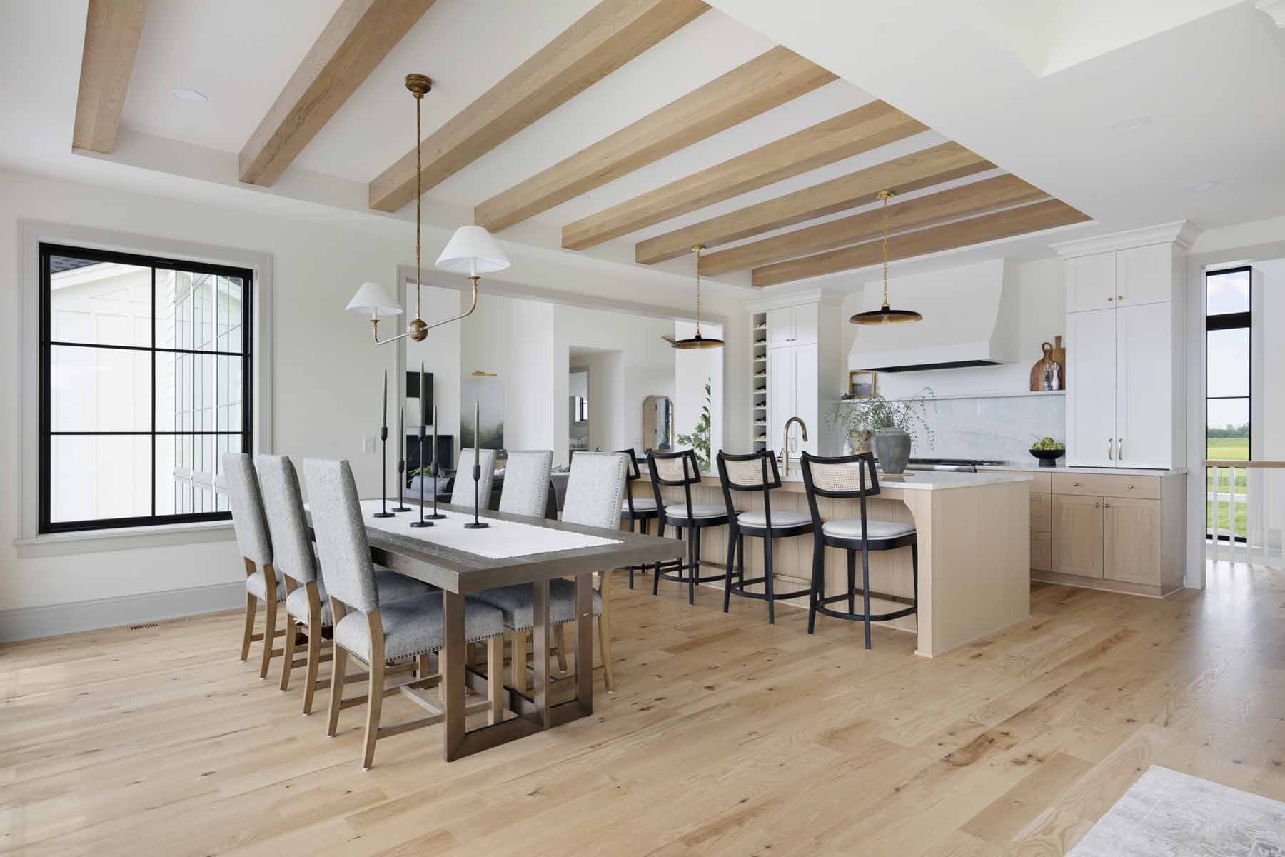 Discover the charm of The Oxbow Ranch home with its modern open-concept kitchen and dining area featuring a wooden floor, beamed ceiling, long dining table for eight, a kitchen island with barstools, and elegant pendant lights.