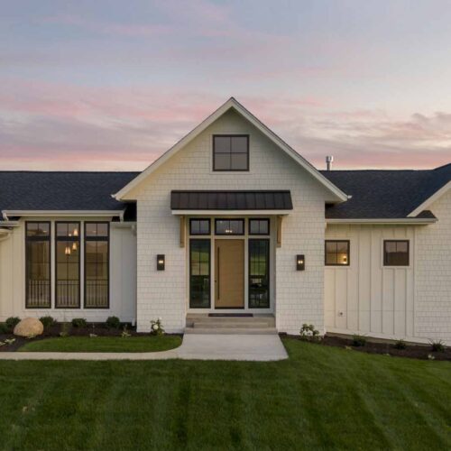 A modern ranch-style house with white siding, large windows, and a landscaped lawn is shown at sunset, epitomizing the charm of properties for sale in this serene area.